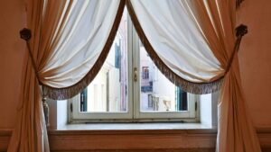 grommet top drapes in michigan hanging drapes by window looking out into european alley way white silky drapes