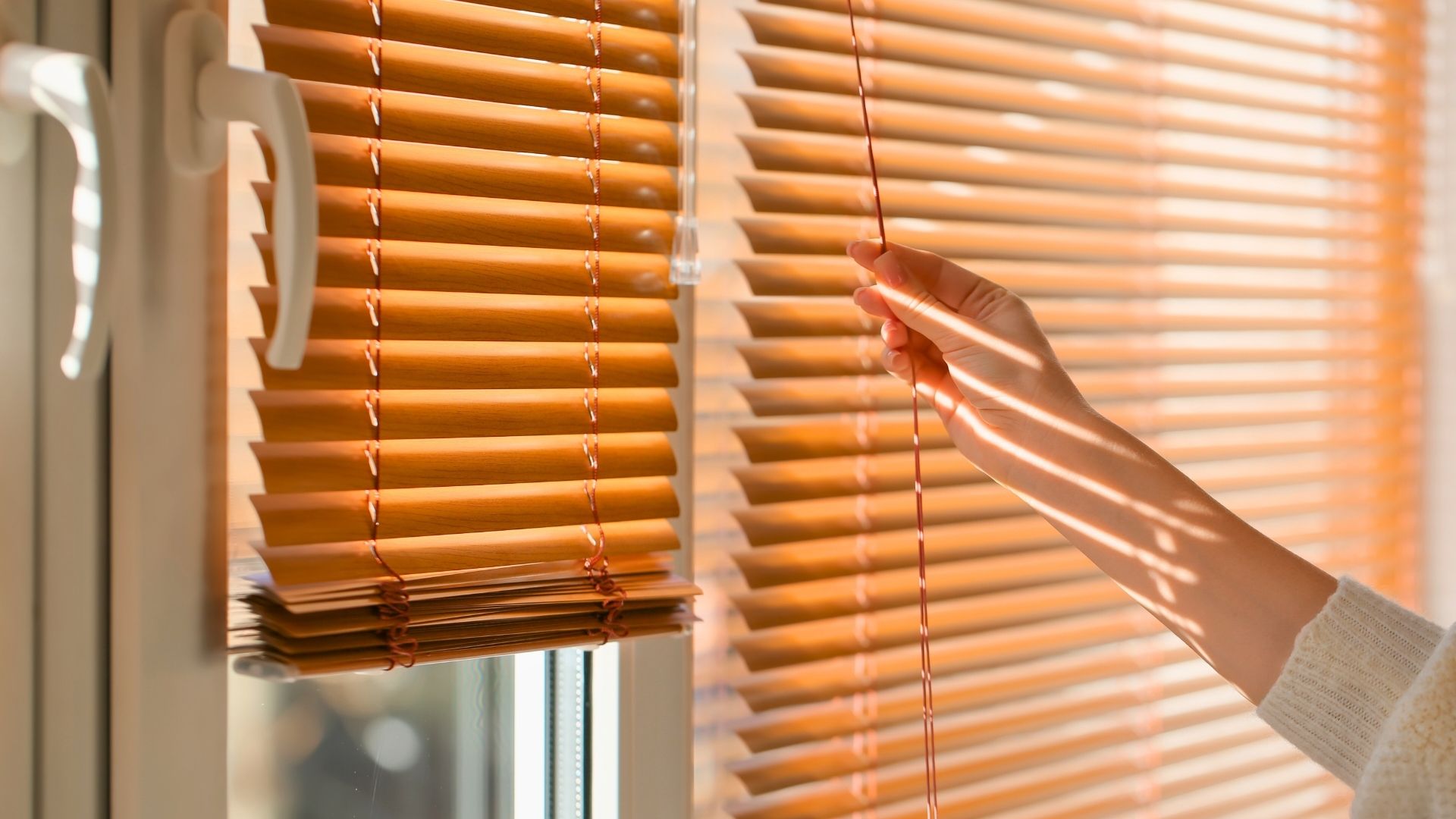 person putting window blinds down to block sun shade and to prep for blind cleaning