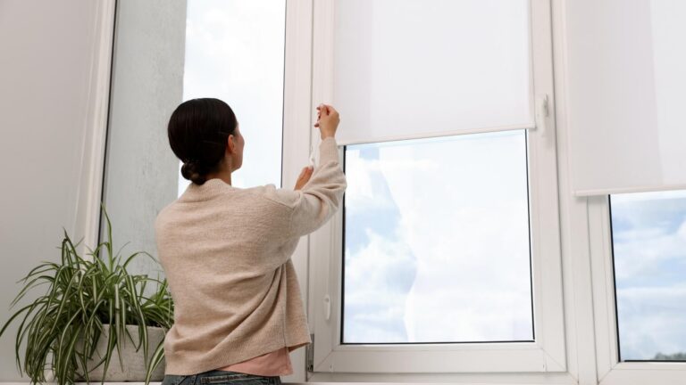 woman in front of window raising the blinds to an open position ready for viewing outside